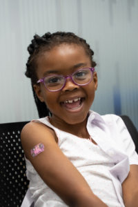smiling young girl with sleeve rolled up showing a plaster on arm after polio vaccination