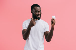 smiling young african american man pointing at condom
