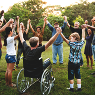Group of people outside holding hands one in a wheelchair and others standing