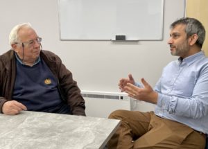 two men sitting talking in GP practice - one is a patient and one is a pharmacist 