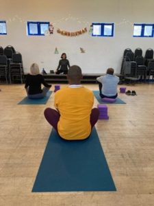 Black man sitting on a yoga mat facing away in a yoga class