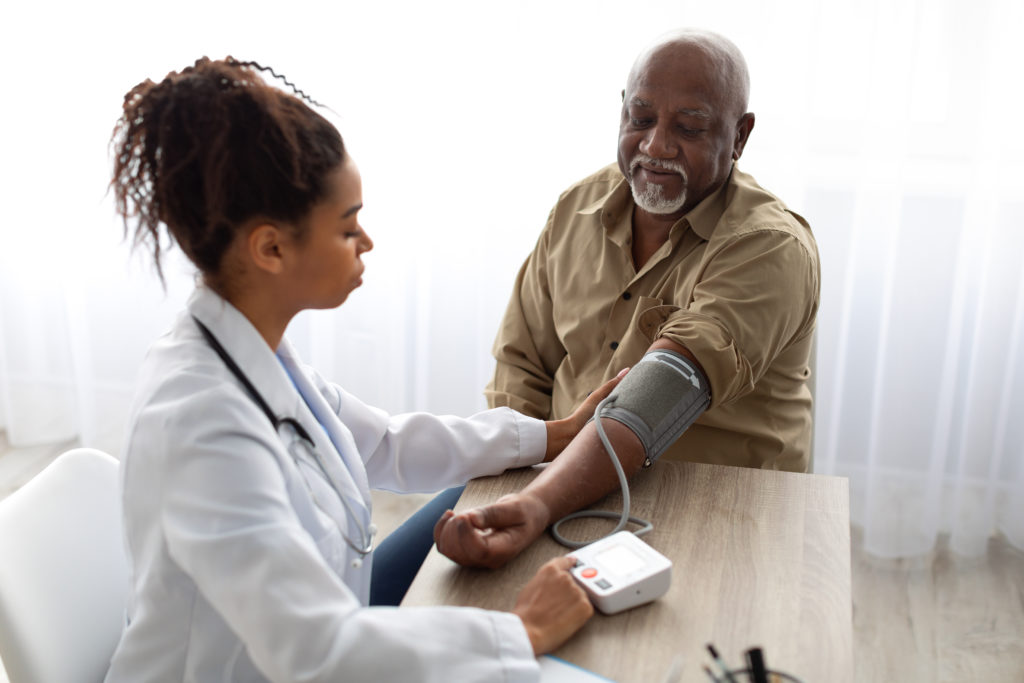 Black female doctor checking elderly black man's blood pressure